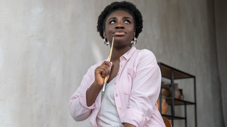 A woman holds a paint brush, thinking