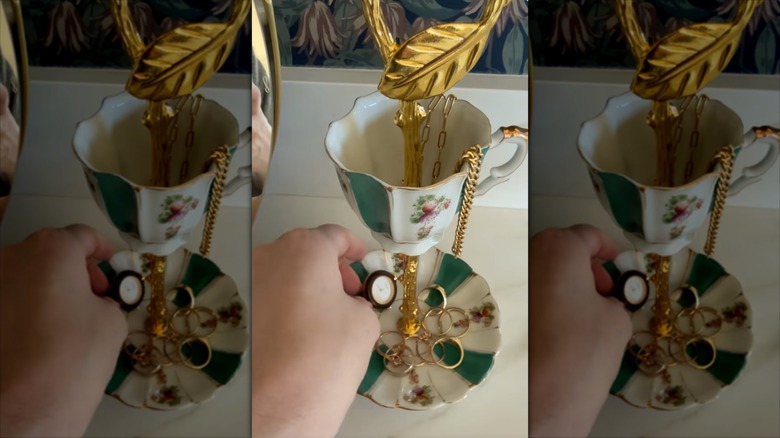 A person places trinkets into a repurposed teacup jewelry stand