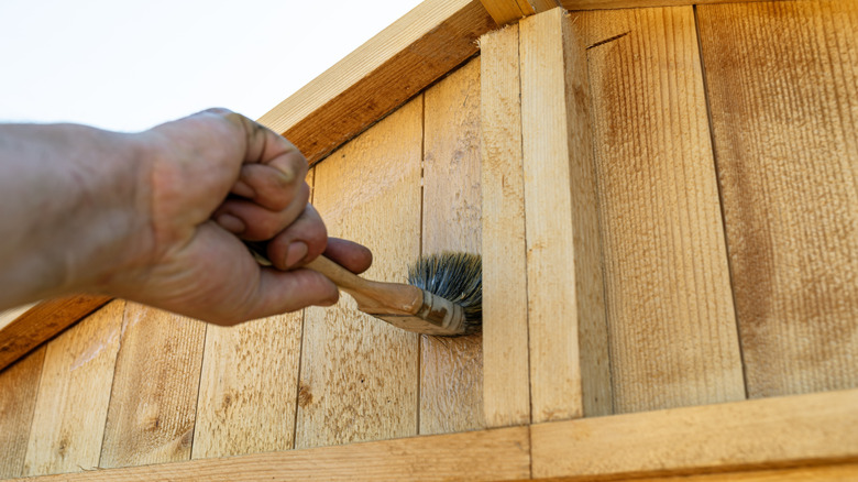 A person painting the outside of a wooden storage shed