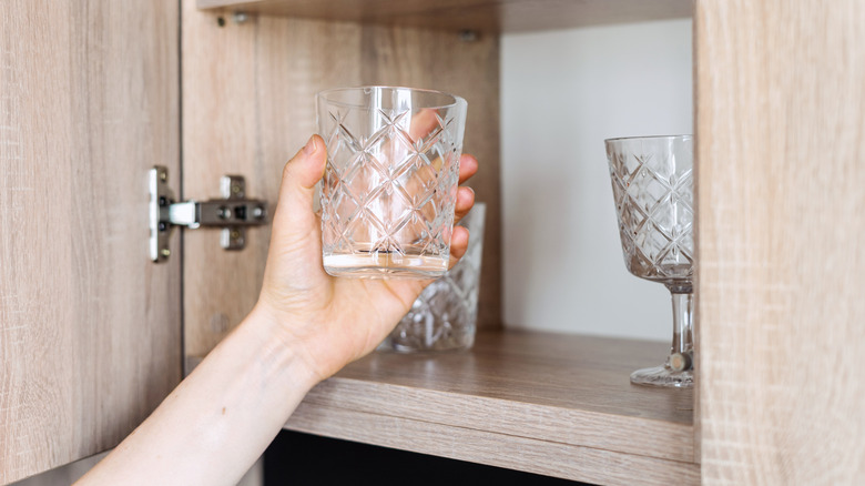 Person taking drinking glass out of cabinet