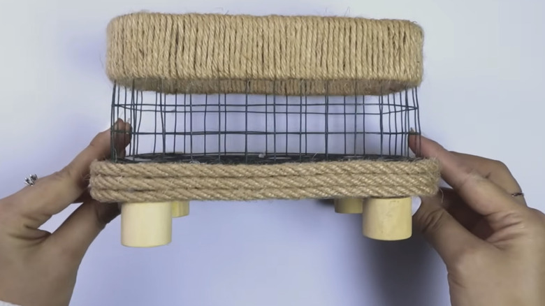 Hands holding DIY countertop basket made from a plastic container lid, wire mesh, and rope