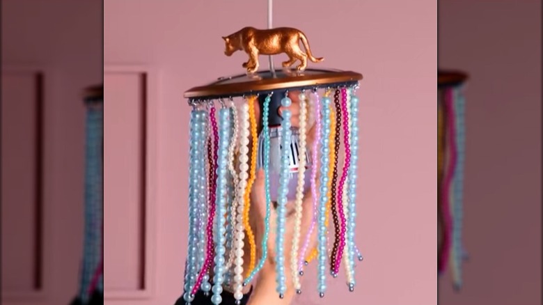 Person screwing a light bulb into a DIY chandelier made from a pot lid with strings of beads