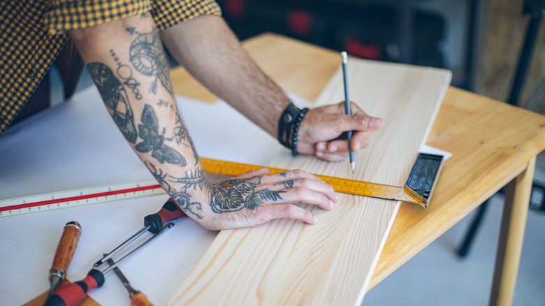 Tattooed person measuring spare wood plank for rustic DIY project