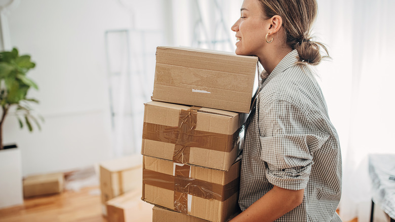 Pretty young woman carrying pile of cardboard boxes