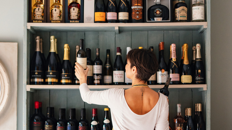A woman reaches for wine bottles on a shelf