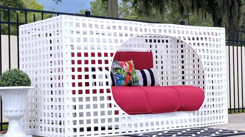 A white daybed with a lattice privacy screening and red cushions
