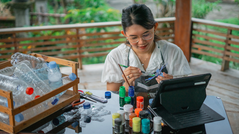 High angle view of woman painting recycled plastic bottle craft.