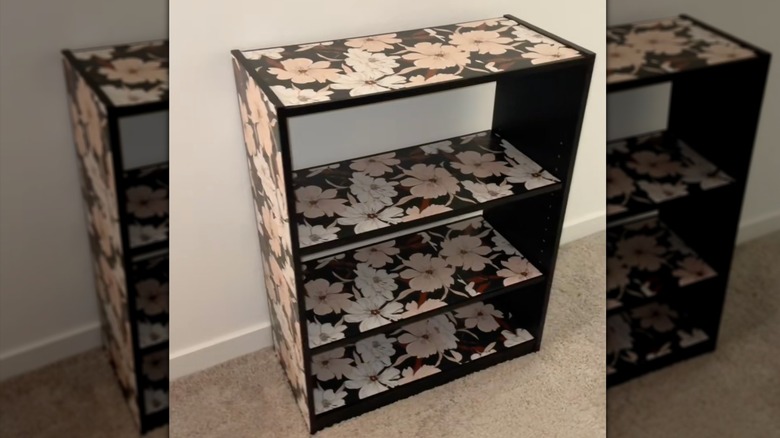 A bookshelf with floral wallpaper on the shelves and sides