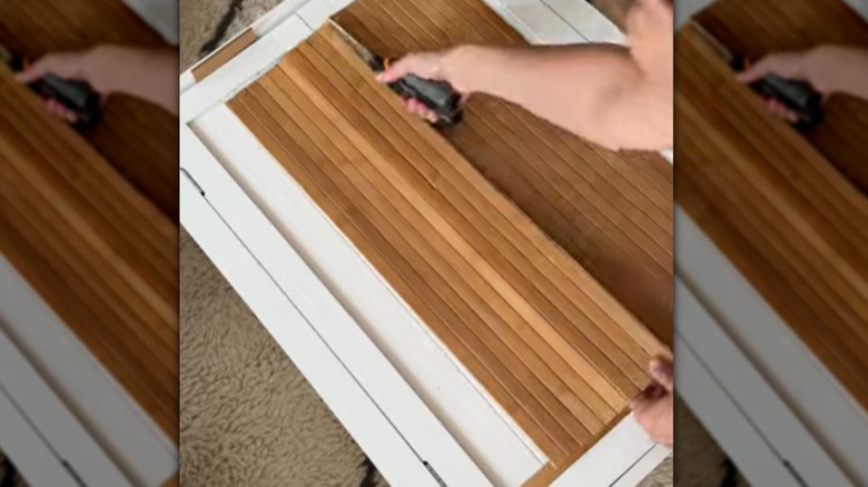 A woman cutting pole wrap to line the front of a white cabinet.