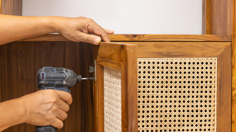 A man adding cane to a wooden cabinet with a drill