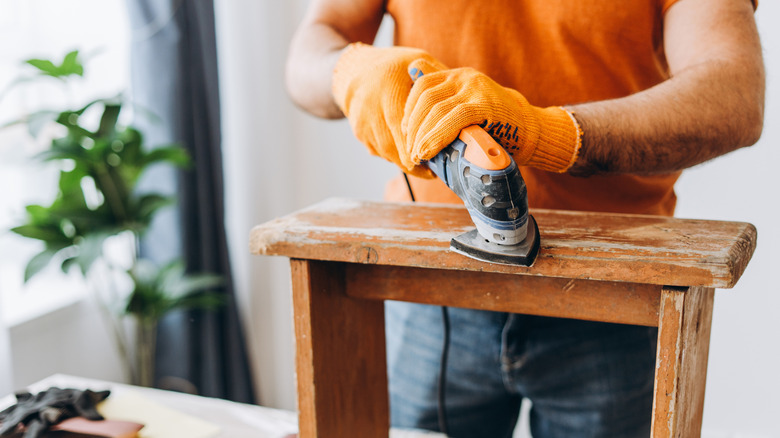 A man sanding an old wooden piece of furniture