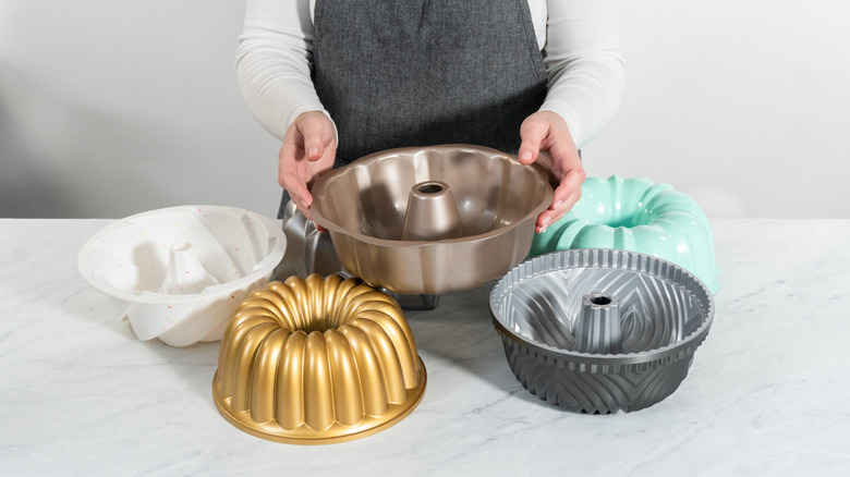 Woman holding up several styles of Bundt pans in different colors on white table