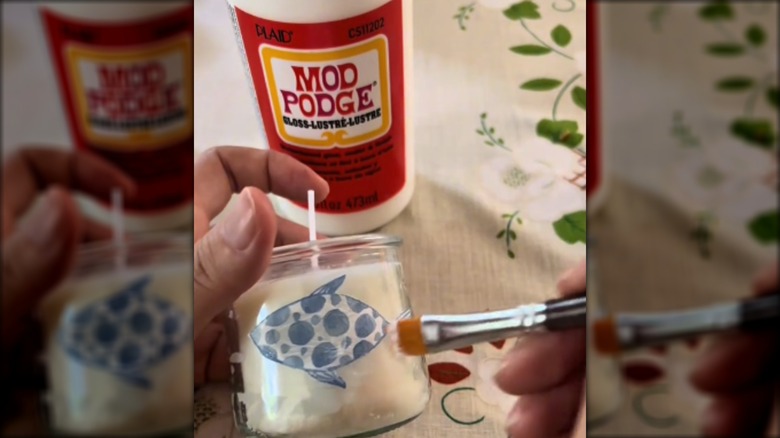 Hands decoupaging a fish onto a candle jar