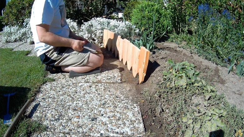 Man installing garden edging made from repurposed wood shaped into stakes