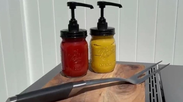 Glass condiment containers with pumps holding ketchup and mustard.