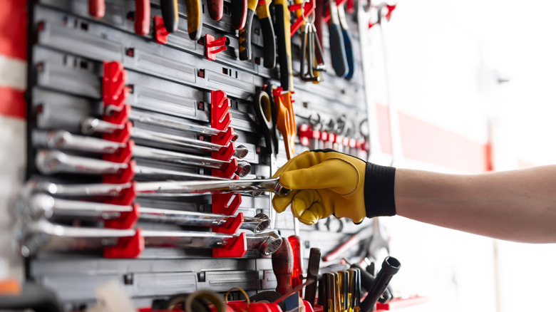Person wearing yellow glove taking wrench off of tool board.