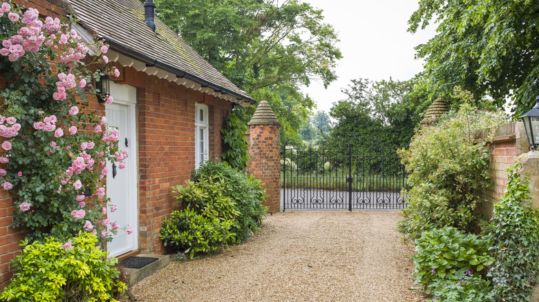 A gravel driveway runs alongside a brick house covered with pink roses