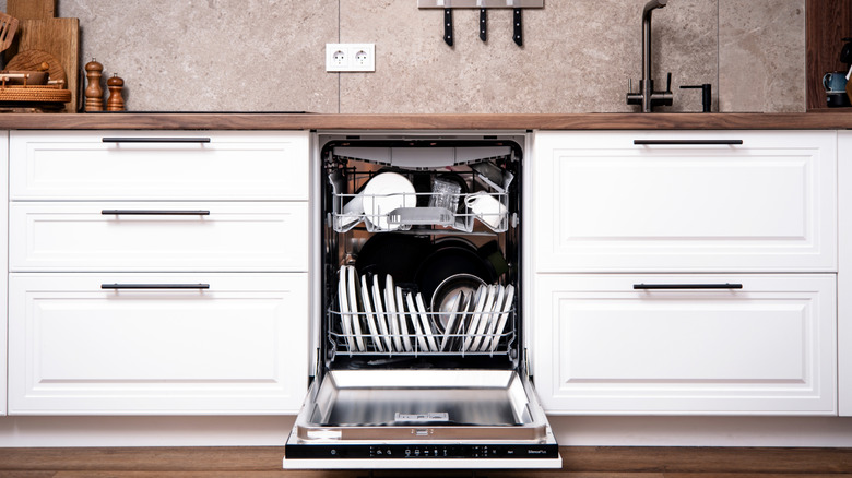 Cluttered and open dishwasher in stylish, contemporary kitchen with white and wood cabinets