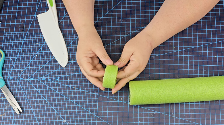 Woman cutting green pool noodle into smaller rings for craft idea