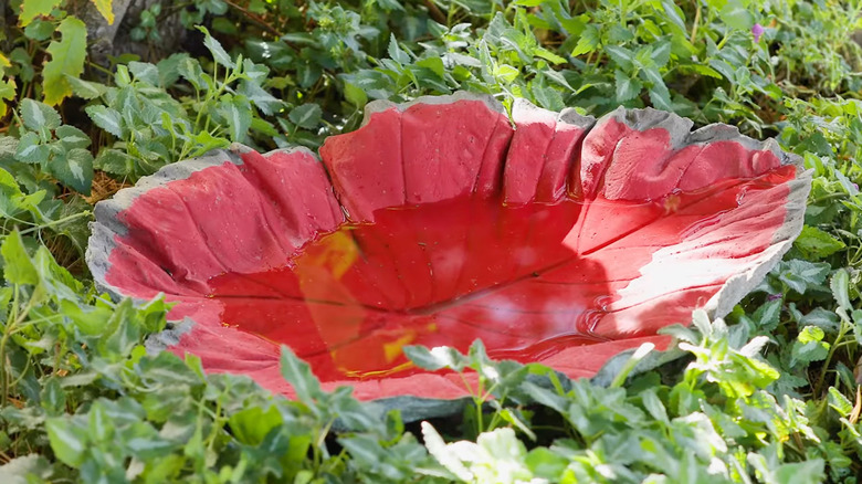 a large red leaf-shaped birdbath surrounded by greenery
