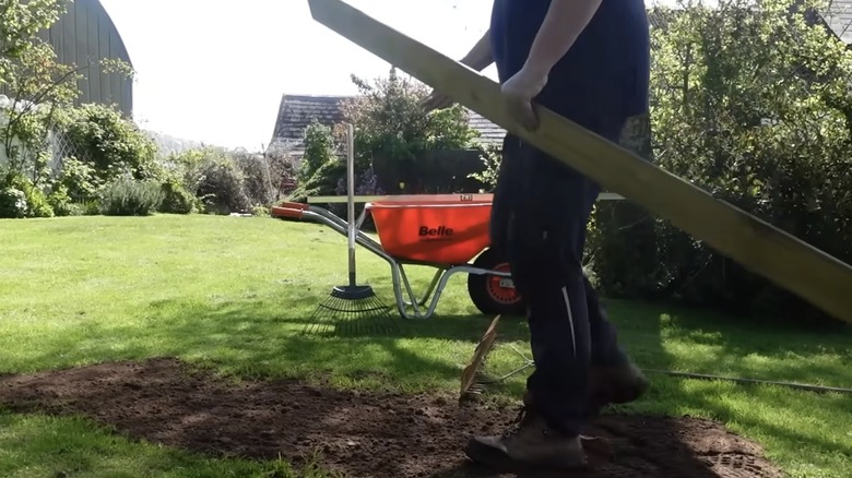 A lawn care expert using a wood plank to assist in fixing a yard low spot