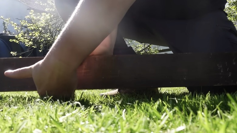 Man using straight board to measure depression in a lawn