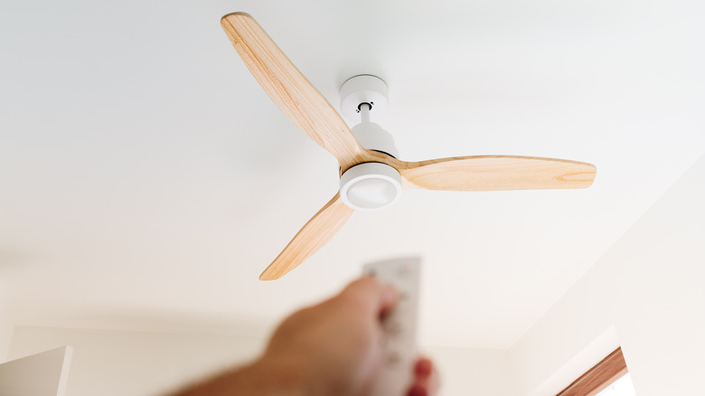 A person using a remote to operate a white and wood ceiling fan