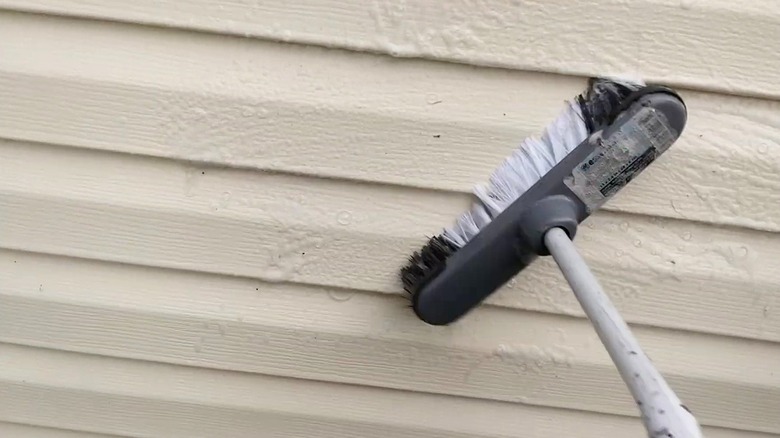 Scrubbing vinyl siding with a long handled brush and soapy water solution
