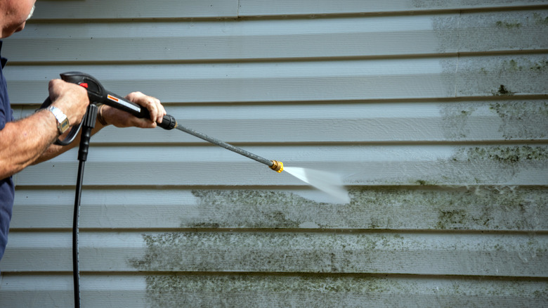 A man using a pressure washer to clean a dirty vinyl siding