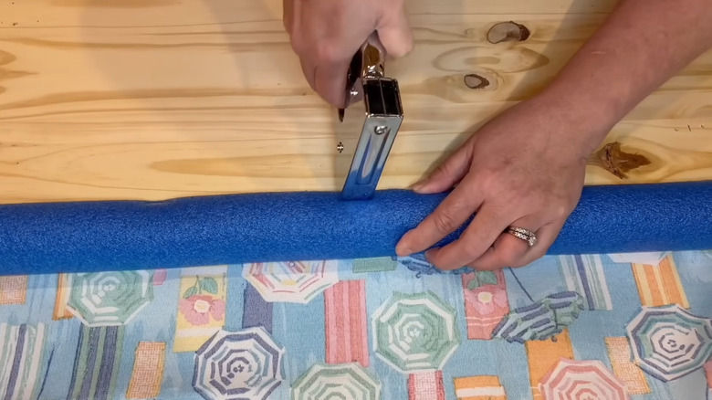Hand stapling apool noodle to wood board
