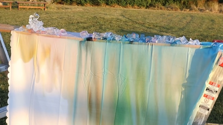 A colored curtain on a wood plank with ice and dyes on top