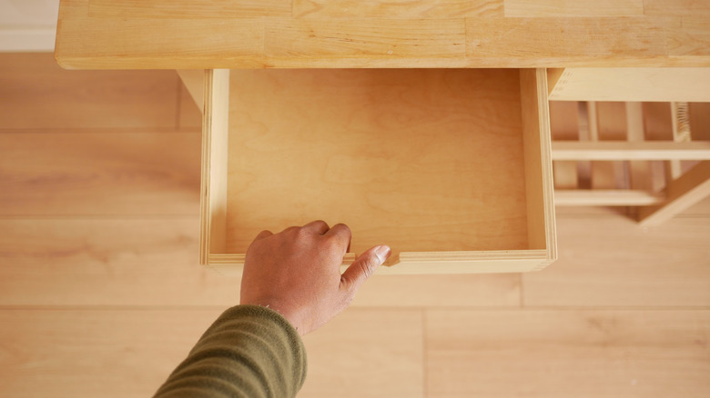 A hand opening a wooden drawer