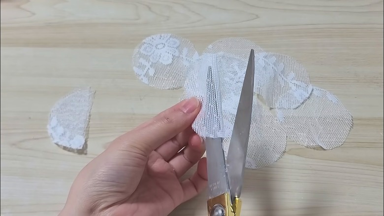 Woman cutting lace fabric with scissors for DIY project over wood table