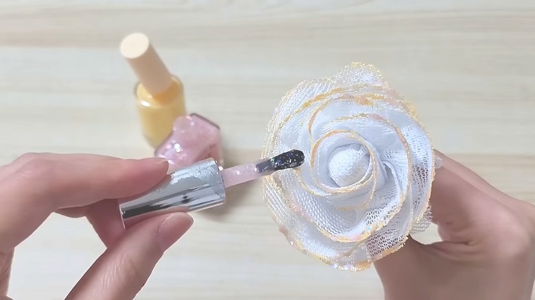 Woman painting handmade lace roses with pale pink and yellow nail polish