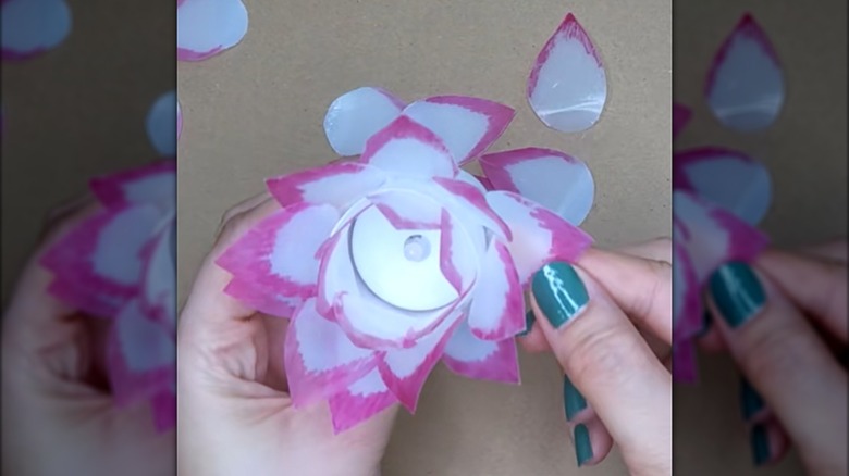 Woman gluing pink milk jug plastic petals around LED candle for countertop decor