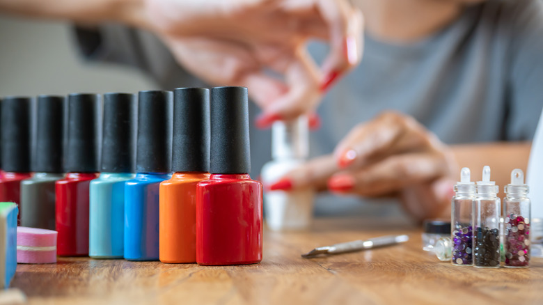 Colored nail polishes with a background of a woman painting her nails on a table