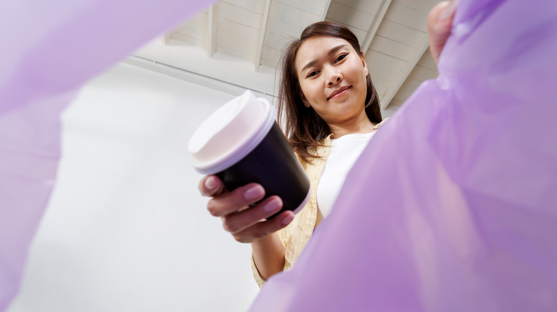 A woman throws a plastic coffee cup into the trash