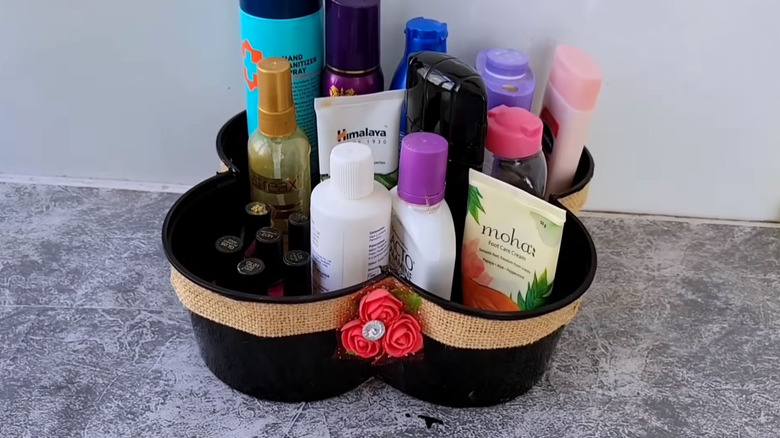 A variety of bath and beauty products sit inside a DIY plastic container bathroom storage solution sitting on a gray countertop