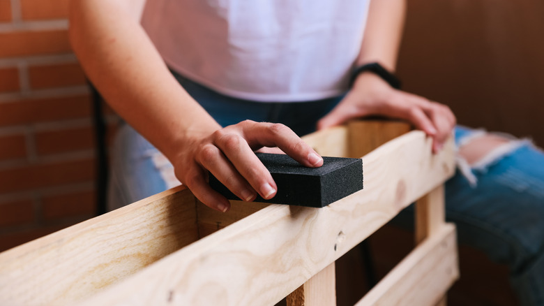 woman sanding a wooden pallet by hand with a sand block