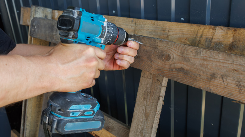 Person driving a screw into a wood pallet