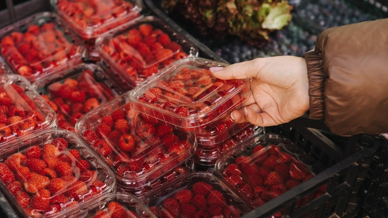 Person selecting a plastic container full of raspberries at the supermarket