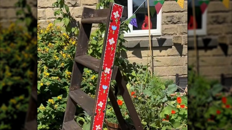 A stained ladder with a painted side with drawn on designs in a garden
