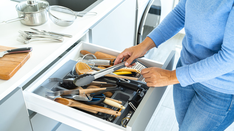 A woman opens a cluttered drawer full of cooking utensils