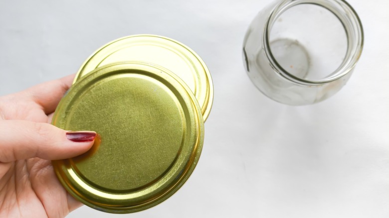 Person hold two Mason jar lids over glass jar
