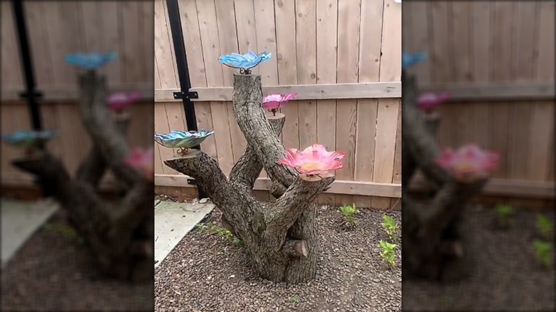Tree stump with multiple branches featuring flower-shaped bird baths attached to them