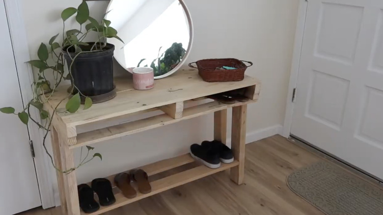 A DIY wood pallet entryway table with a mirror, a plant, a candle, and a basket on top