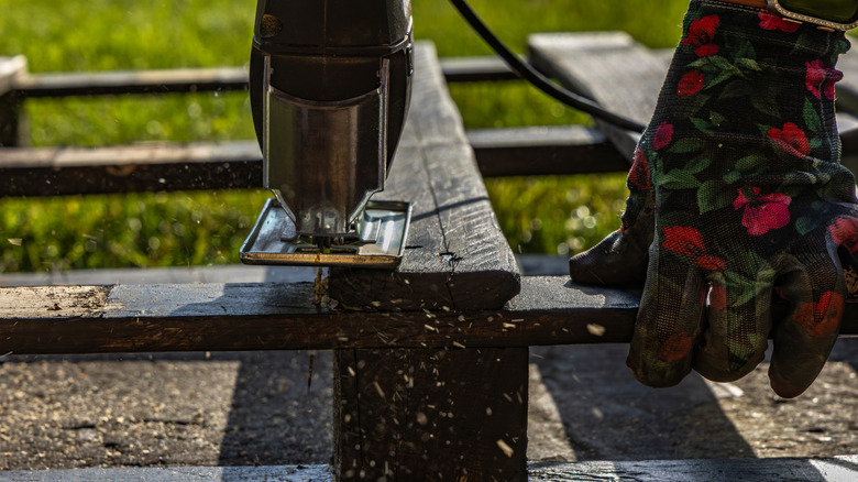 A person wearing floral gloves using a corded saw to cut a pallet wood