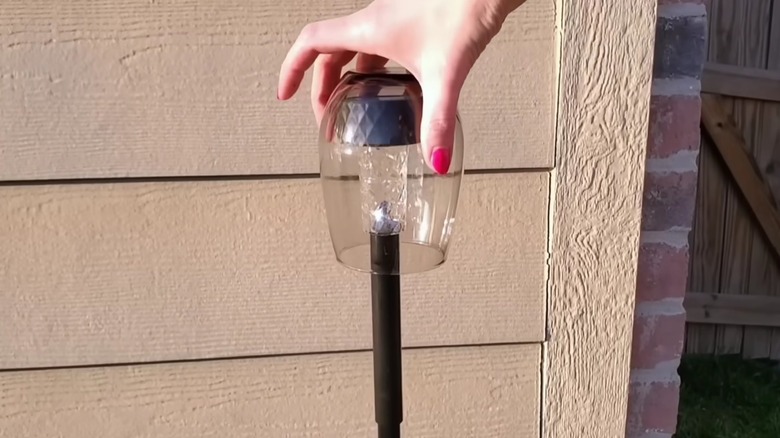 Manicured hand setting up a DIY Dollar Tree stake light using solar lights and repurposed wood dowels and wine glasses