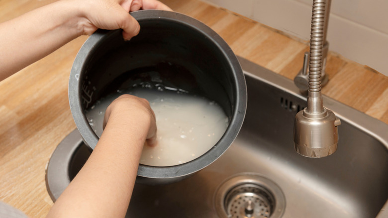 Hands reaching into a pot filled with rice water