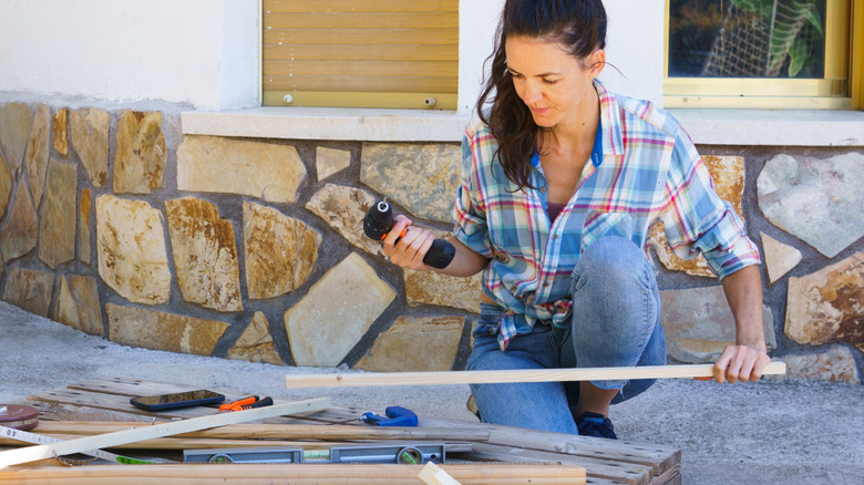 A woman works on a wood pallet project outside a house